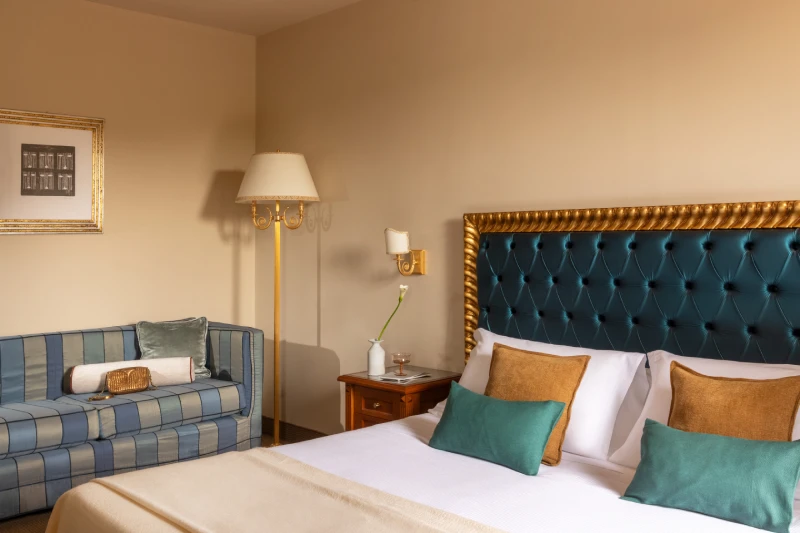 Close-up of bed with blue tufted headboard, sea-toned cushions and cosy lounge corner in Sarzana, Liguria - Sarzana Park Hotel, BZAR hotels in Liguria